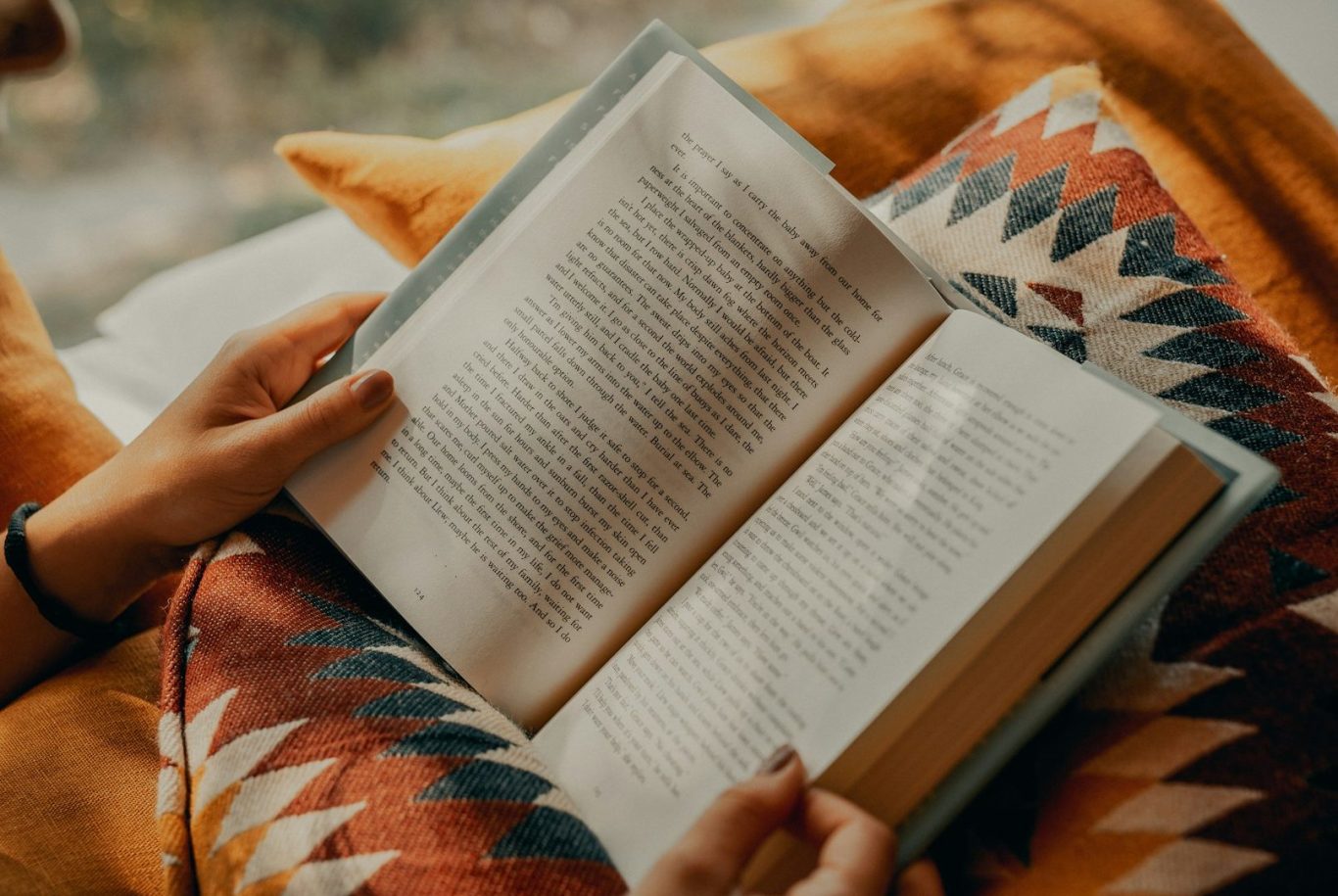 Reading a book A person reading a book while seated on a patterned blanket.