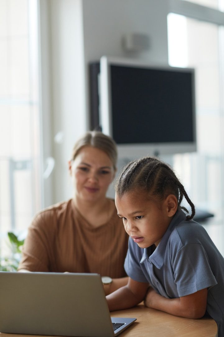 Girl and woman on laptop A woman and a child engaged with a laptop at a table in a bright room.