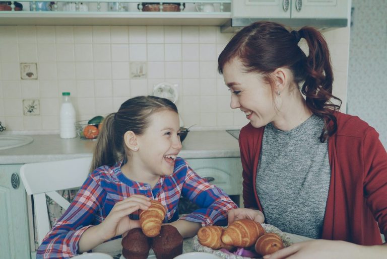Woman and girl with snacks A woman and a girl smiling at each other, surrounded by baked goods at a kitchen table.