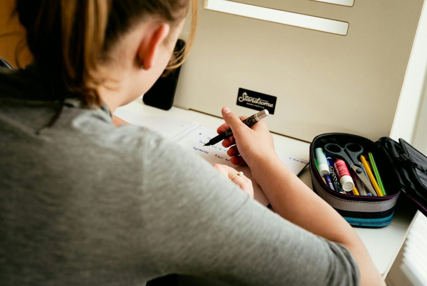 Teenager studying A person writes on paper at a desk with a pencil case and colourful pens.