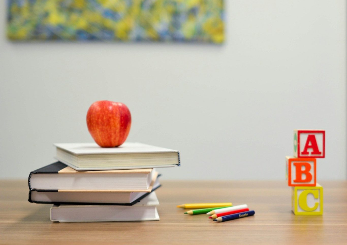 Stack of books Red apple placed on top of stacked books beside colourful letter blocks.