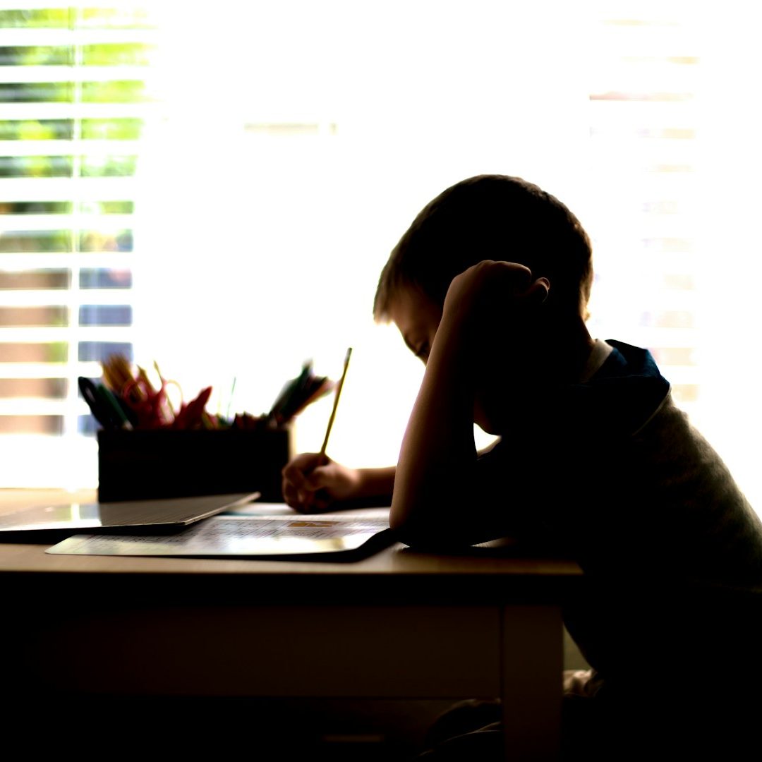 A silhouetted child sitting at a desk, writing, with a window in the background.