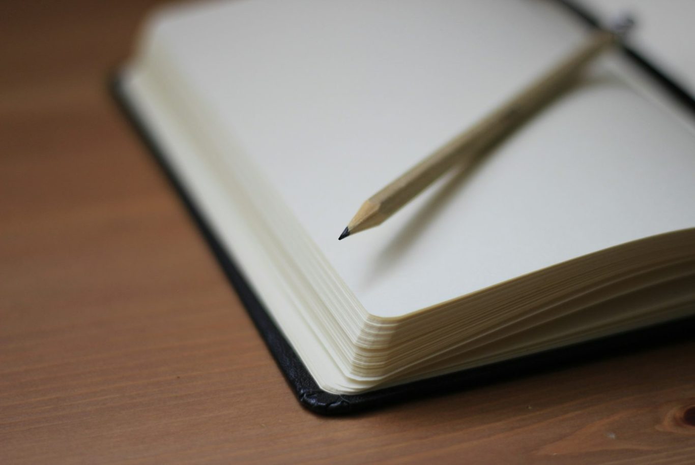 Notebook A blank notebook with a pencil resting on top, placed on a wooden surface.