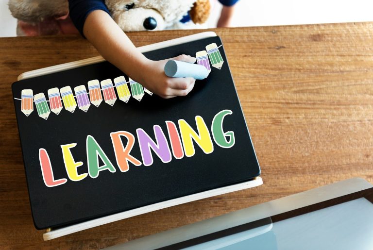 Chalk writing Child's hand writing "LEARNING" in colourful chalk on a blackboard.