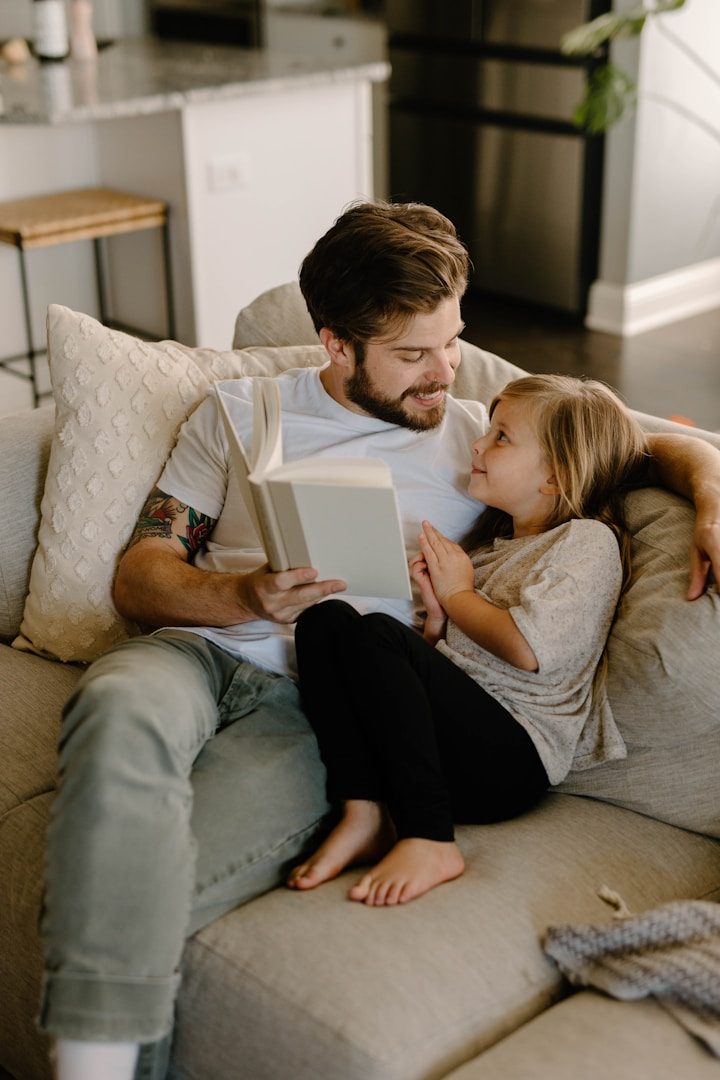 Father reading with daughter A father reading a book to his daughter on a sofa, both smiling and relaxed.