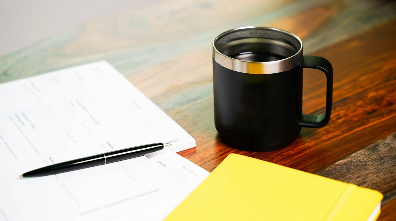Coffee and notebook A black mug beside a yellow notebook and a pen on a wooden table.