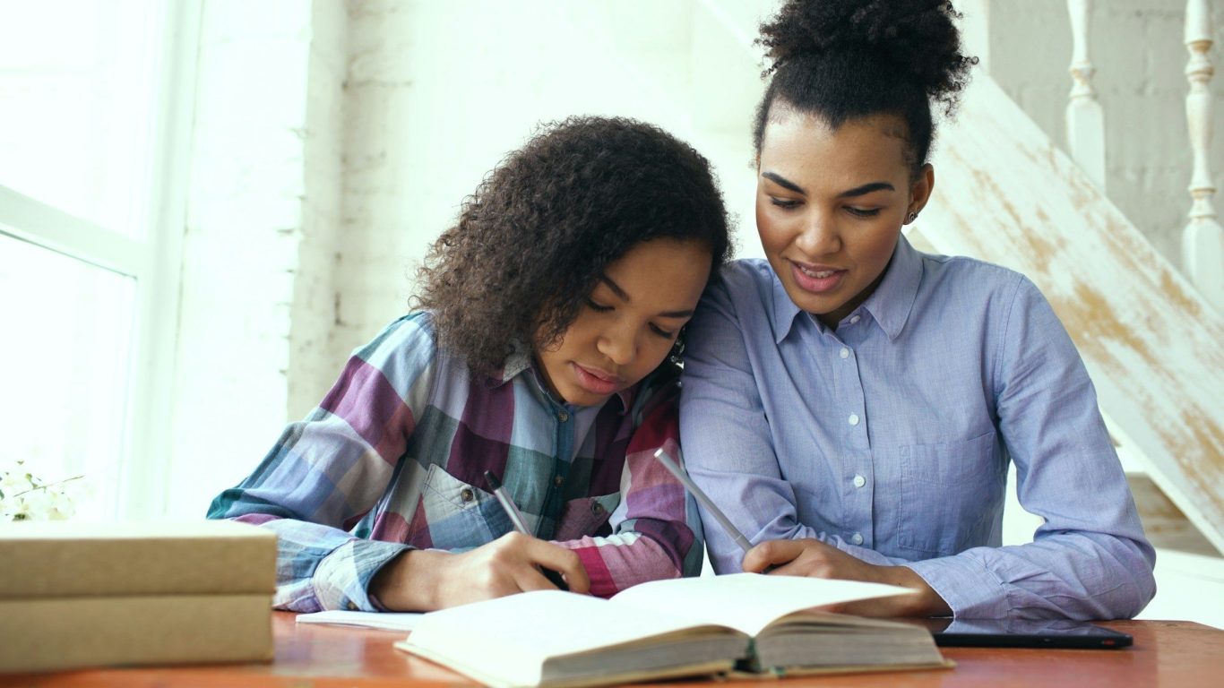 Woman and teenager studying Two women studying together, one writing in a book while the other watches attentively.