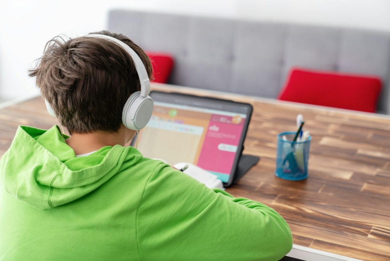 Child with headphones on laptop Person wearing headphones sitting at a desk with a laptop, focused on the screen.
