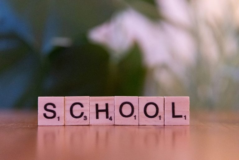 School letters Scrabble tiles spelling the word "SCHOOL" against a blurred green background.